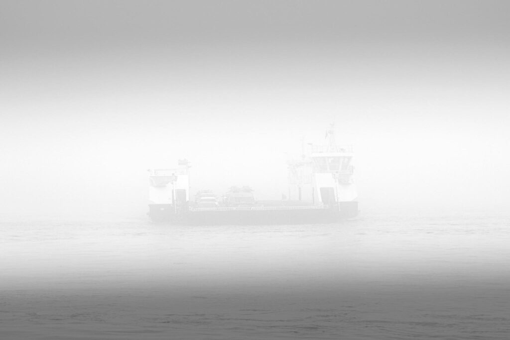 Balsa solitária quase desaparecendo em meio à neblina sobre um rio, em cenário silencioso e indefinido, simbolizando lembranças que se tornam difusas e marcas sutis deixadas por relações ao longo do tempo.