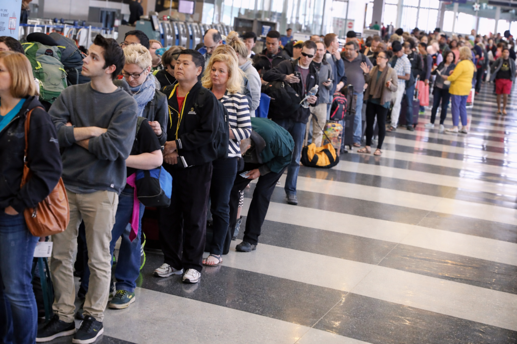 Pessoas em fila dentro de um aeroporto aguardando atendimento, representando a experiência coletiva do cotidiano e a vida compartilhada em espaços públicos.